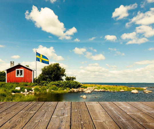 Rotes Schwedenhaus am See mit Holzsteg und blauem Himmel. 