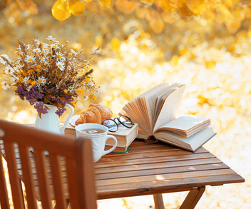 Gartenstuhl mit Holztisch und einem aufgeschlagenen Buch. 