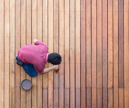 Mann streicht Holzboden mit Holzlasur.